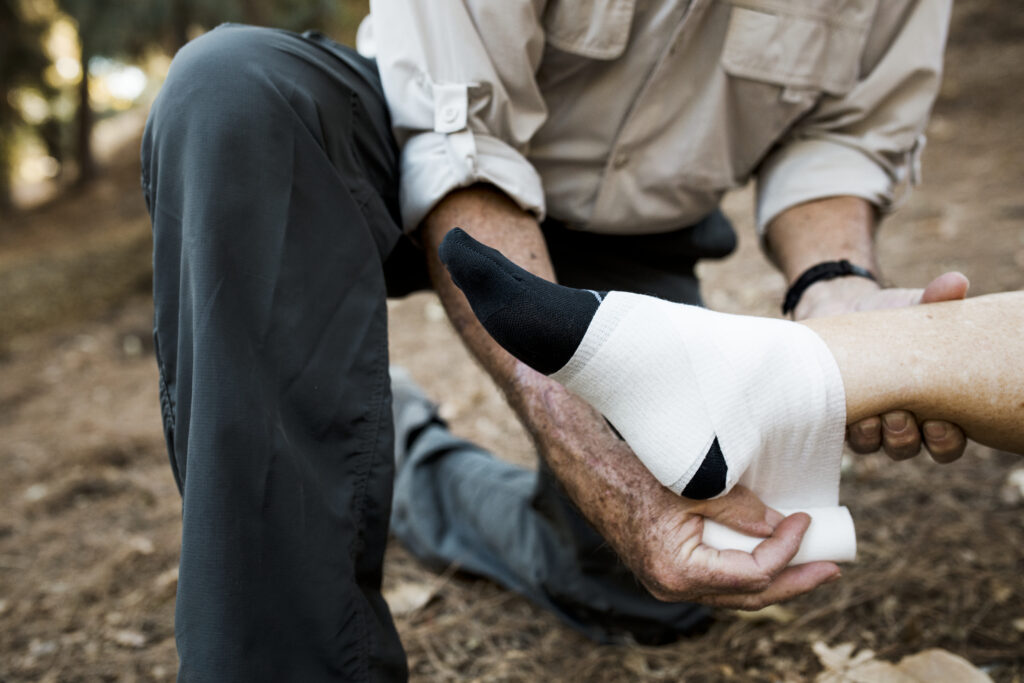 Older man carefully wrapping a bandage around his wife's injured foot during a hike.