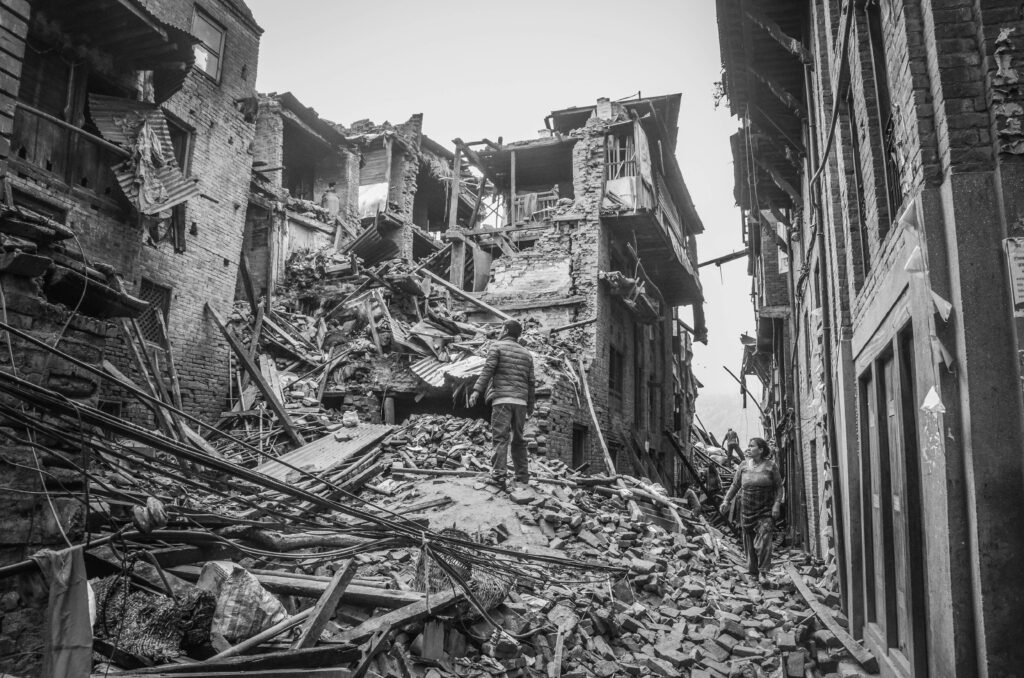 A black and white photograph showing the devastating impact of an earthquake in a city, with collapsed buildings and people navigating through the rubble.