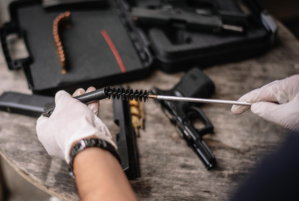 Person cleaning a handgun barrel with a bore brush, with firearm case and ammunition on the table.