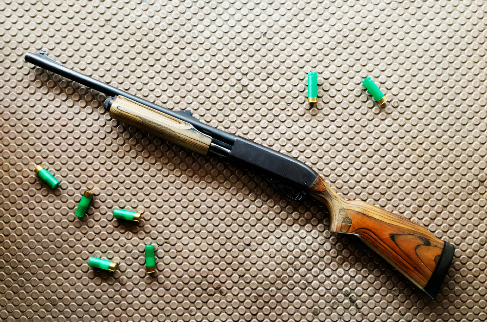 Shotgun with wooden stock and scattered green shells on a textured surface.