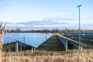 Solar panels installed in an open field with clear skies and a fenced perimeter.