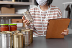 Person inspecting canned goods and organizing an emergency food storage stockpile with a clipboard, highlighting proper prepping practices.