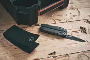 Leatherman Wave+ multi-tool placed on a wooden surface near a black tool case, surrounded by screws and wood shavings.