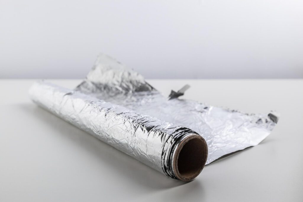 A roll of aluminum foil partially unrolled on a white surface, showcasing its reflective and versatile material.