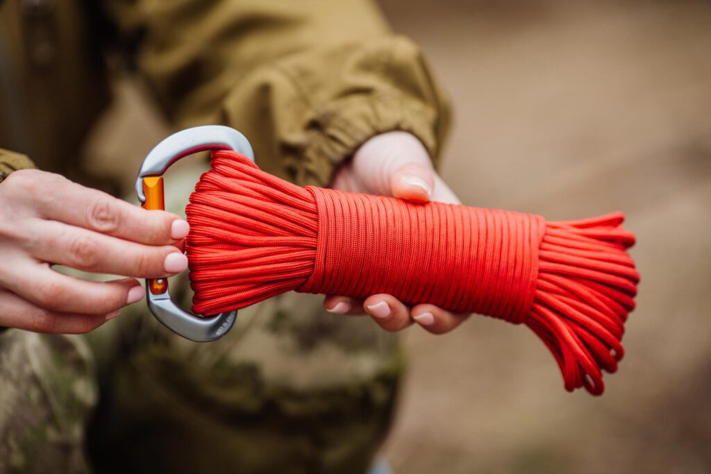 Hands holding a bright red paracord wrapped neatly with a carabiner, showcasing its durability and versatility in outdoor and survival settings.