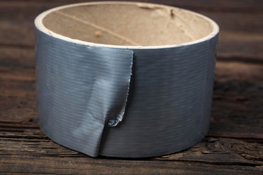 A roll of gray duct tape with a slightly peeled edge sitting on a rustic wooden surface, showcasing its durability and versatility for survival purposes.