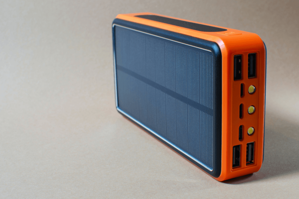 Portable orange solar power bank with multiple USB ports, ideal for charging devices during winter power outages.