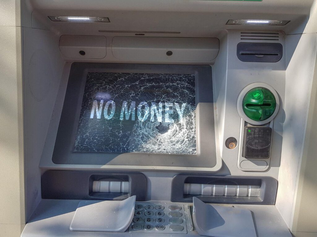 A broken ATM with a shattered screen displaying "NO MONEY," signaling economic collapse and societal instability—one of the key warning signs of civil unrest.