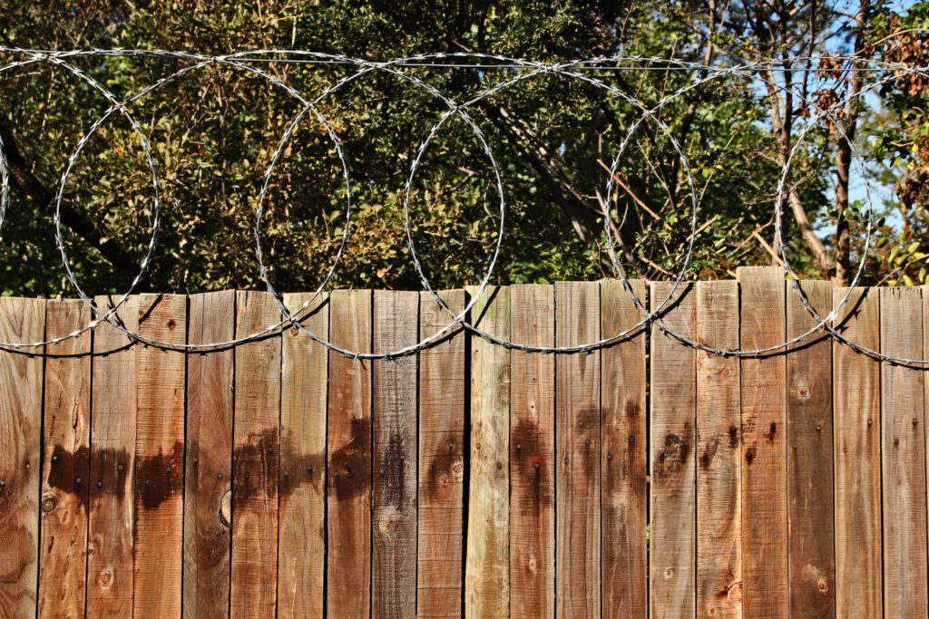 A tall wooden fence topped with barbed wire, serving as a security measure to deter intruders and protect the property.