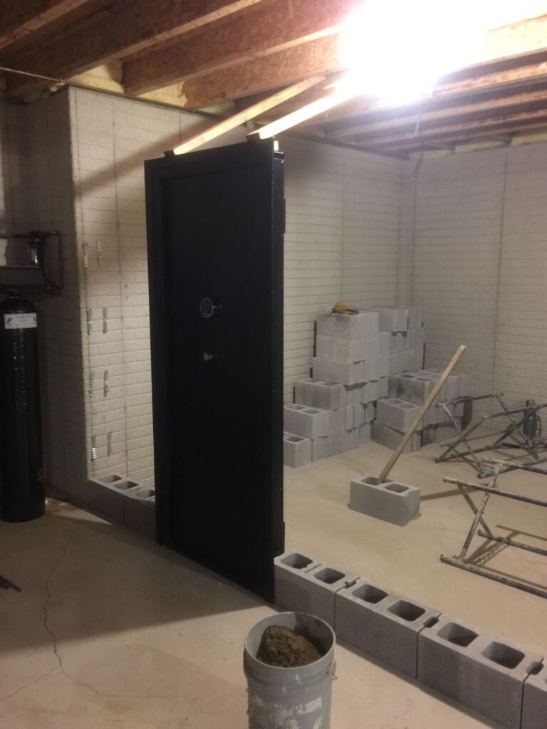 A partially constructed safe room with a reinforced steel door, cinder block walls, and construction materials, showcasing a secure space for emergencies.