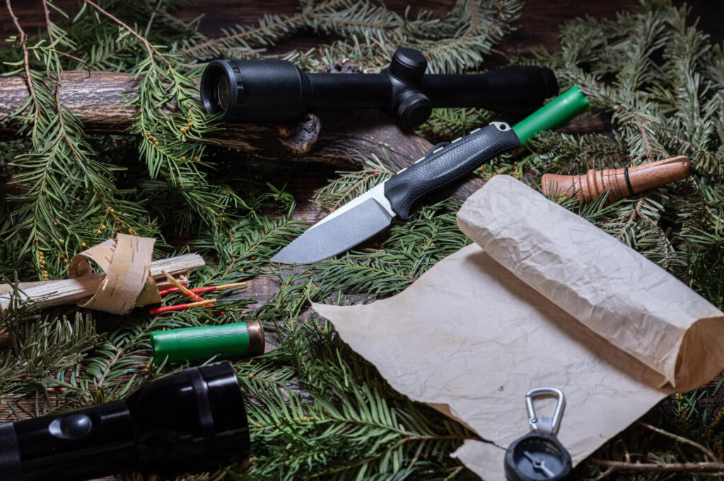 Various survival items laid out on pine branches, including knife, flashlight, compass, and map