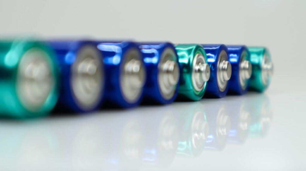 Close-up of blue and green AA batteries lined up on a reflective surface