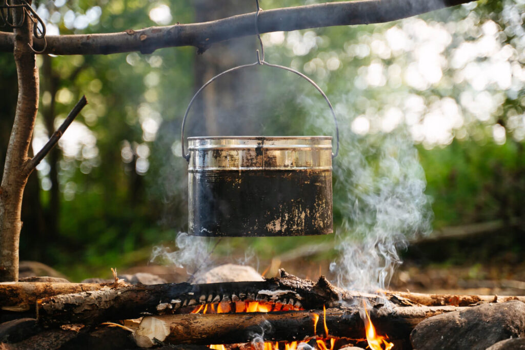 Metal pot boiling water over a smoky campfire in the forest