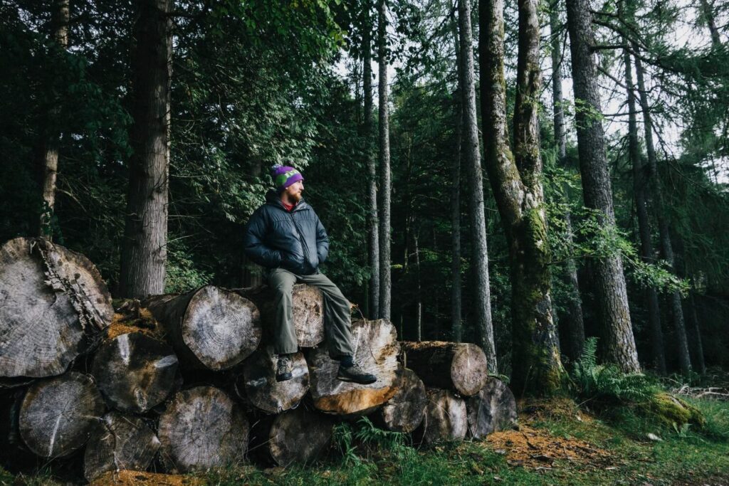 Man sitting calmly on logs in the forest, pausing to think during wilderness situation