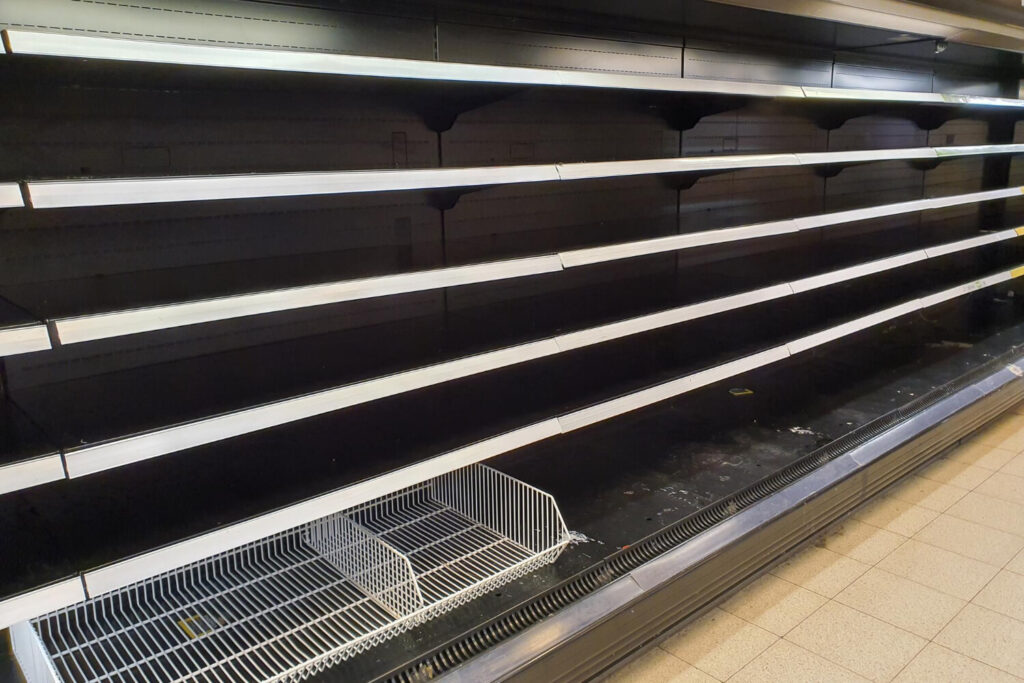 Empty grocery store shelves with missing food items, symbolizing supply chain breakdown during global conflict.