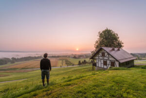 Man looking over rural farmland and cabin at sunrise, symbolizing off-grid living and self-reliance