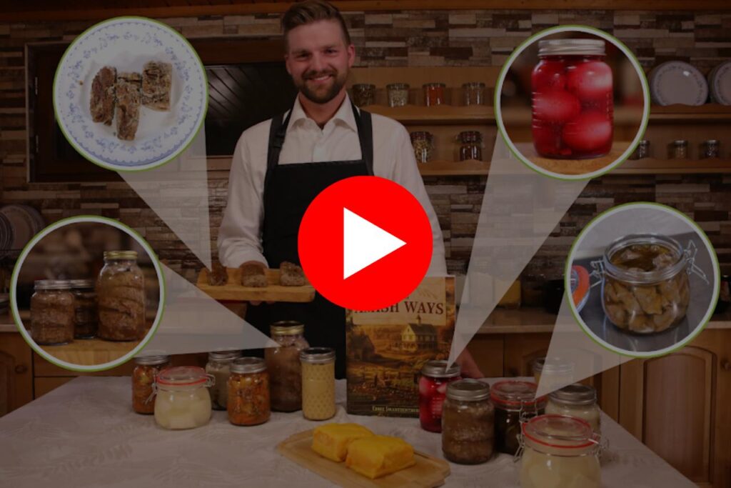 Man presenting traditional Amish preserved foods and The Amish Ways book in a rustic kitchen setup.


