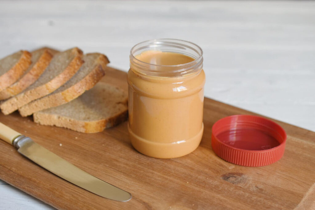 Peanut butter jar and canned proteins like tuna, Spam, and beans — essential shelf-stable survival foods.