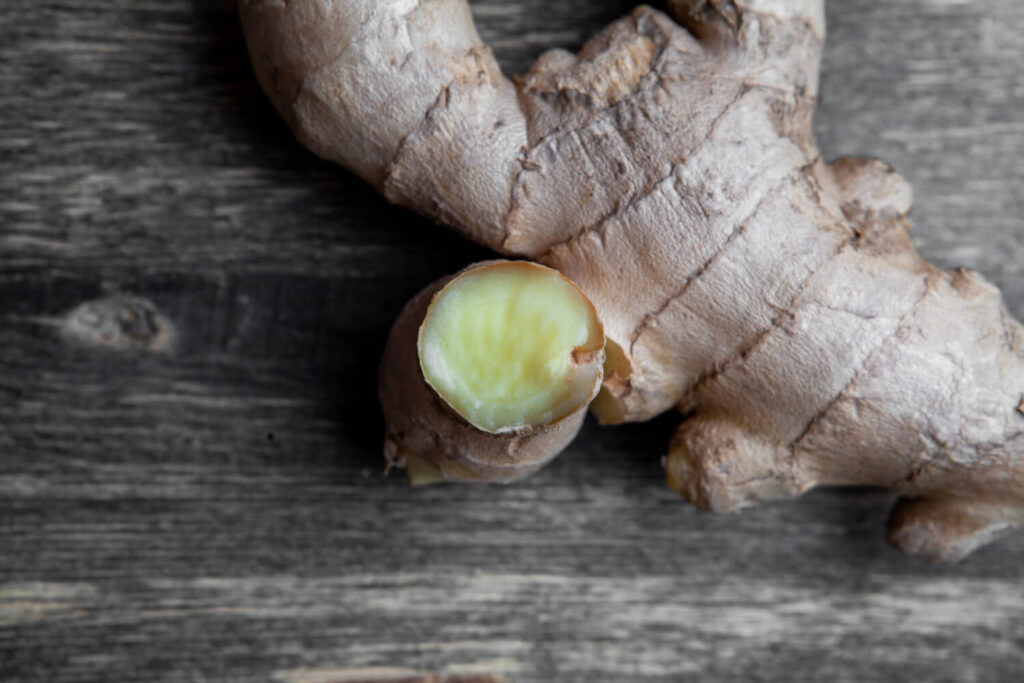 Fresh cut ginger root on a rustic wooden table, used for natural nausea relief and herbal remedies.