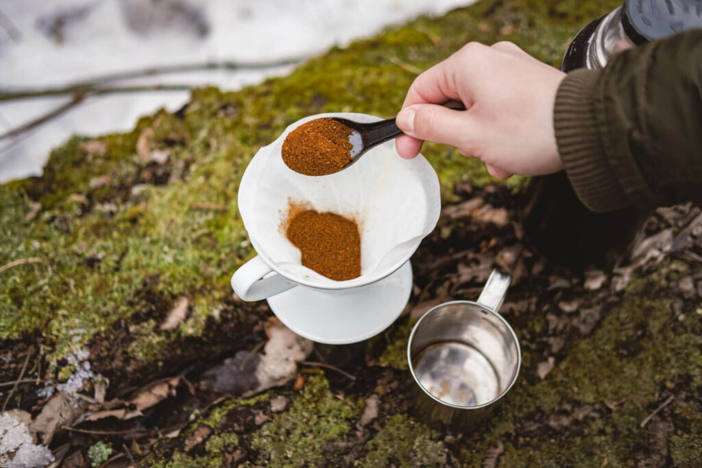 Prepper brewing coffee outdoors with ground beans during blackout survival.
