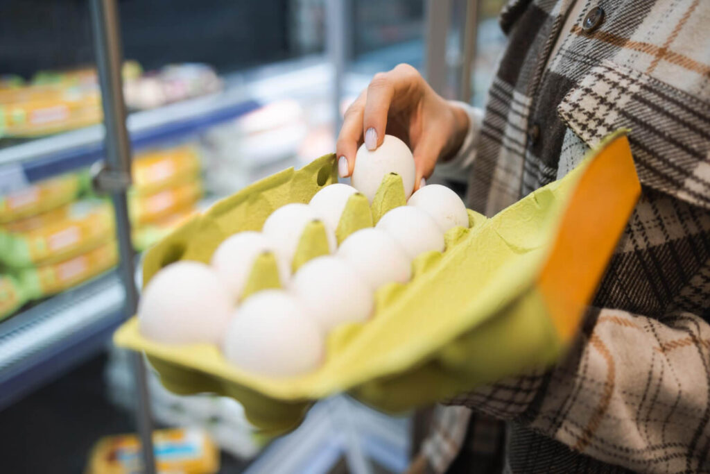 Shopper picking up fresh eggs in a grocery store during panic buying before a blackout.