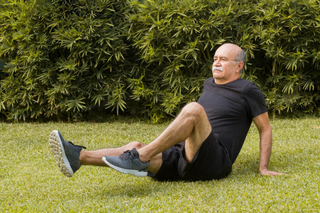 Older man doing joint mobility exercises on grass to stay physically prepared after 50.

