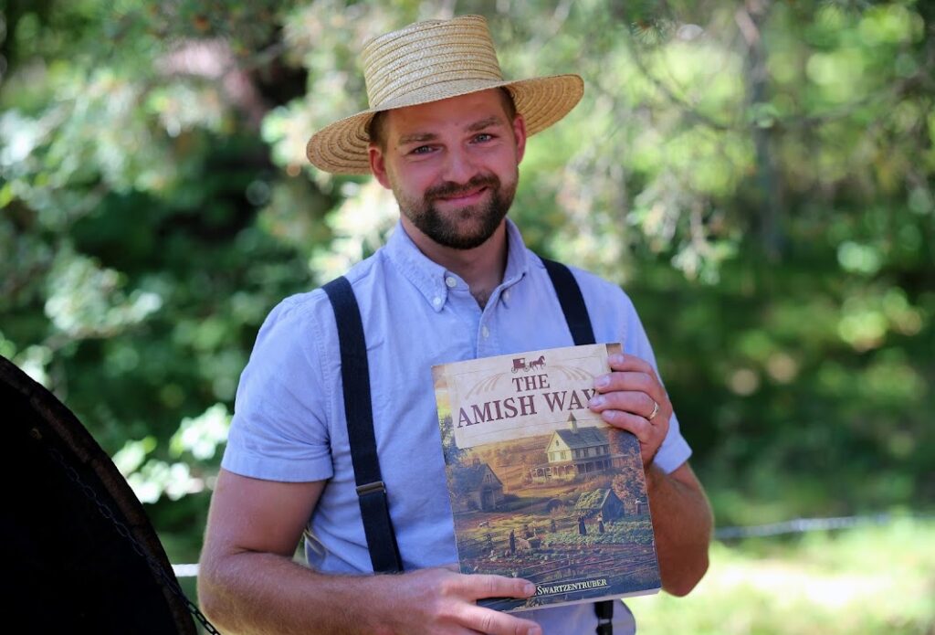 Amish man holding "The Amish Ways" survival book outdoors

