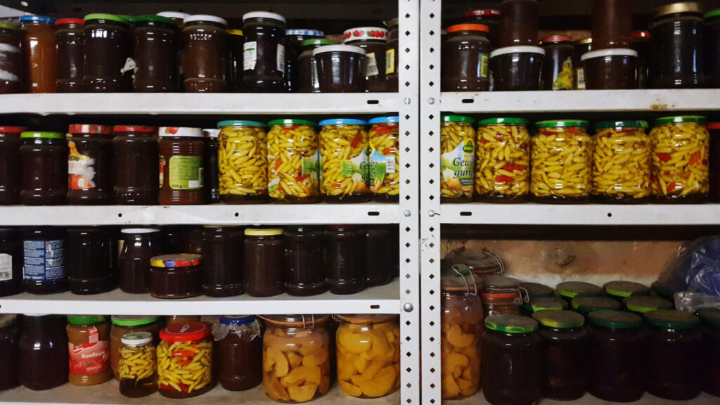 Basement pantry shelves filled with home-canned jars—pickles, preserves, and fruit—long-term food storage for winter blackouts.