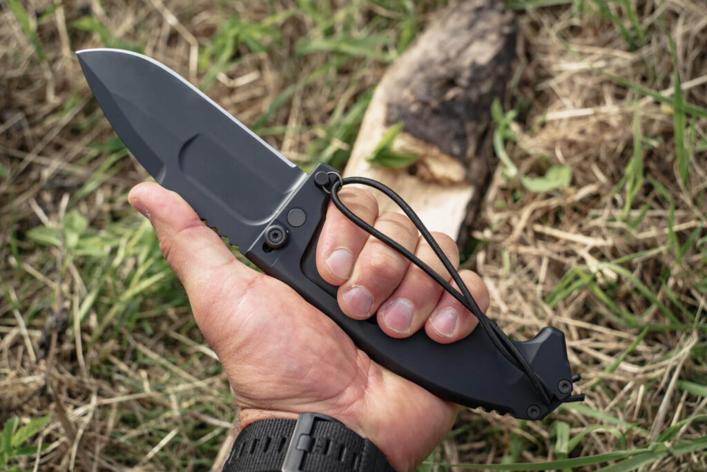 Hand holding a survival knife in a hammer grip outdoors for safe cutting and carving.