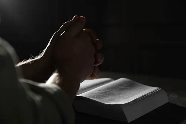 Person praying over an open Bible representing biblical preparedness and faith during uncertain times in David’s Shield survival guide
