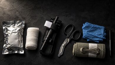 Bleeding control kit laid out on a dark surface: hemostatic gauze, rolled gauze, tourniquet, trauma shears, nitrile gloves, emergency pressure bandage and marker