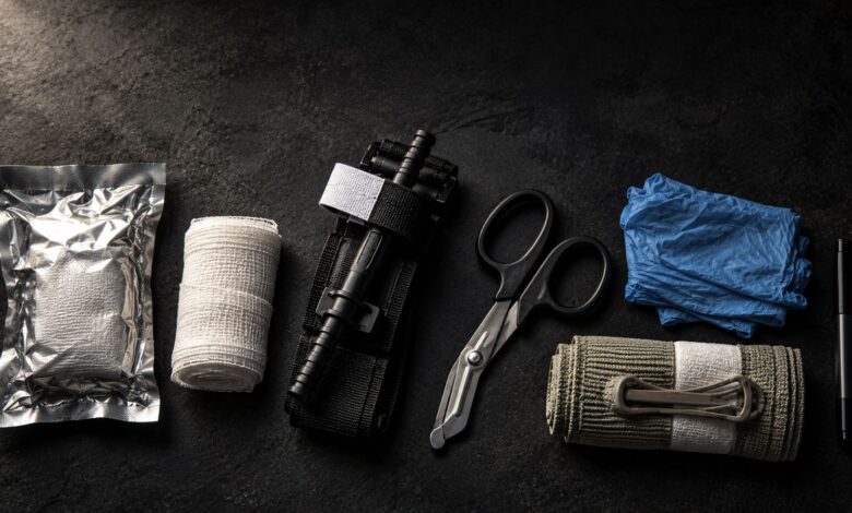 Bleeding control kit laid out on a dark surface: hemostatic gauze, rolled gauze, tourniquet, trauma shears, nitrile gloves, emergency pressure bandage and marker