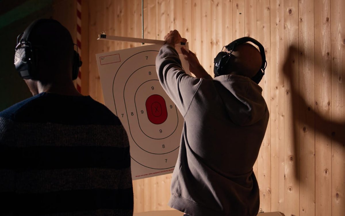 Two men setting up a paper target for indoor firearm training, without any visible weapon