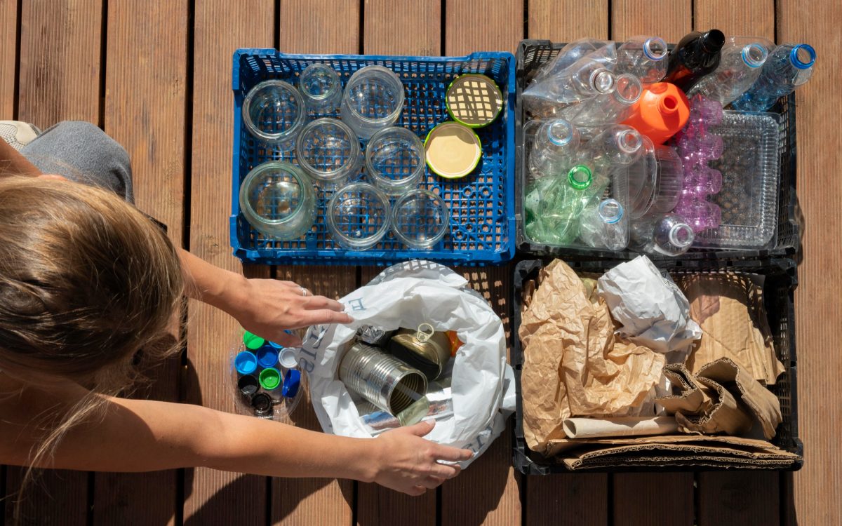 Overhead view of a woman sorting recyclables, including glass jars, plastic bottles, aluminum cans, and paper, highlighting the potential for survival uses.