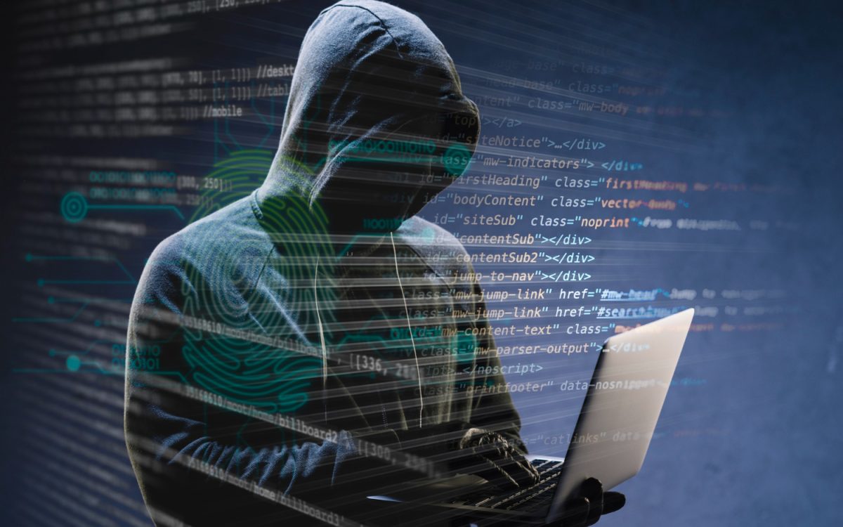 Hacker in a hoodie holding a laptop surrounded by code, symbolizing cybersecurity threats.