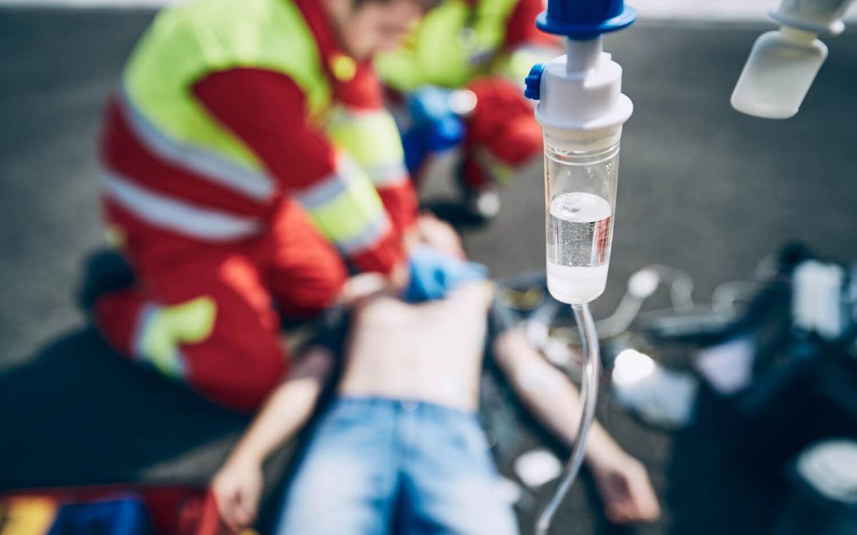 Paramedics performing CPR on a man during a medical emergency with IV drip in focus.