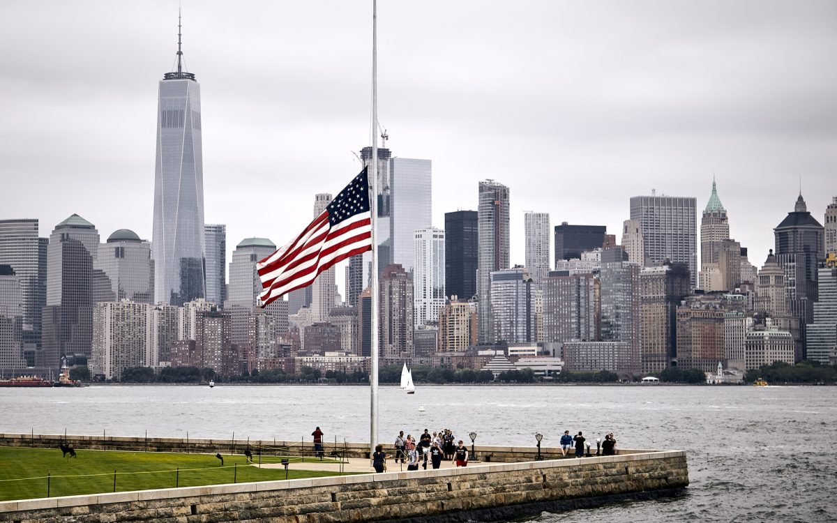 American flag flying at half-staff with the Manhattan skyline in the background, symbolizing urban vulnerability and the need for thoughtful survival planning.