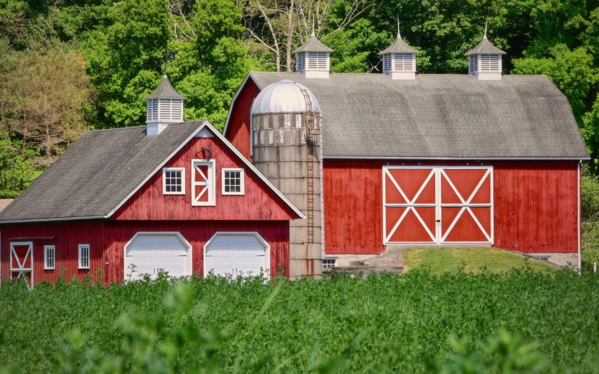 Amish-style red timber-frame barn with silo and X-braced doors in a rural landscape.