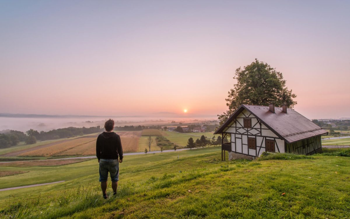 Man looking over rural farmland and cabin at sunrise, symbolizing off-grid living and self-reliance