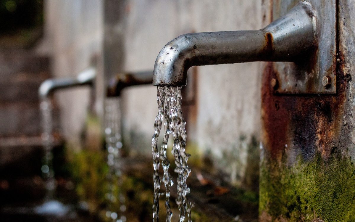 Close-up of water flowing from a rusted outdoor faucet, emphasizing the importance of clean water access and filtration.