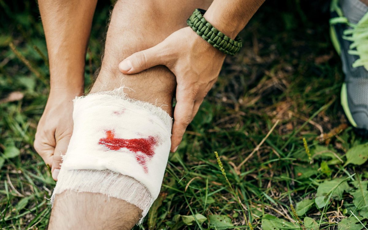 Close-up of a hiker bandaging a bleeding knee injury in the wilderness.