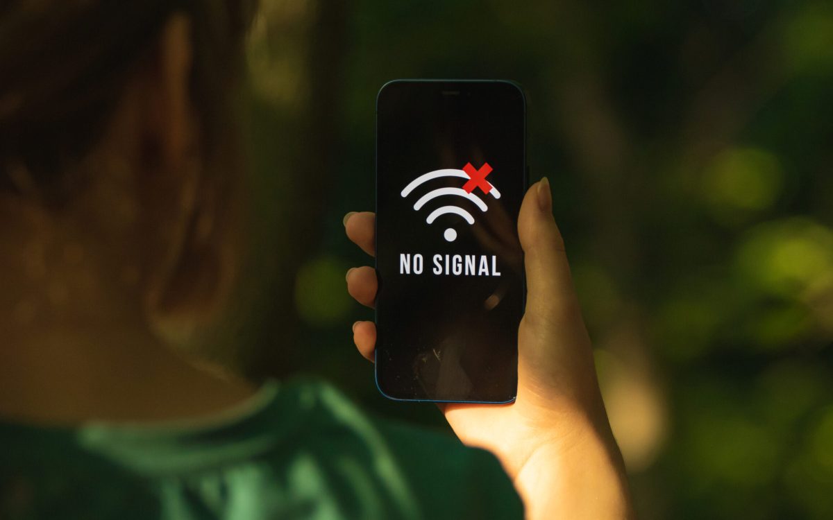 Mobile phone displaying 'No Signal' screen held by a woman in a forest, representing communication failure in emergencies.